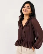 Chocolate brown crinkle chiffon blouse with a ruffle neckline, front tie detail, fabric-covered buttons, peplum hem, and long balloon sleeves displayed in a flat lay.